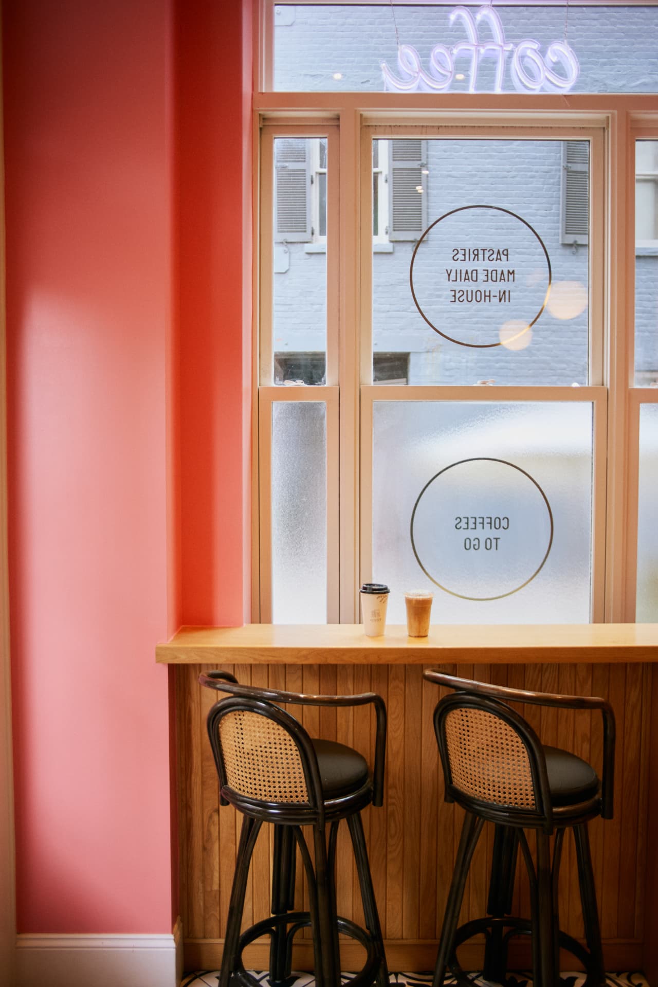 Interior window bar with two cane stools, a coral wall, and a hot and an iced coffee on the counter