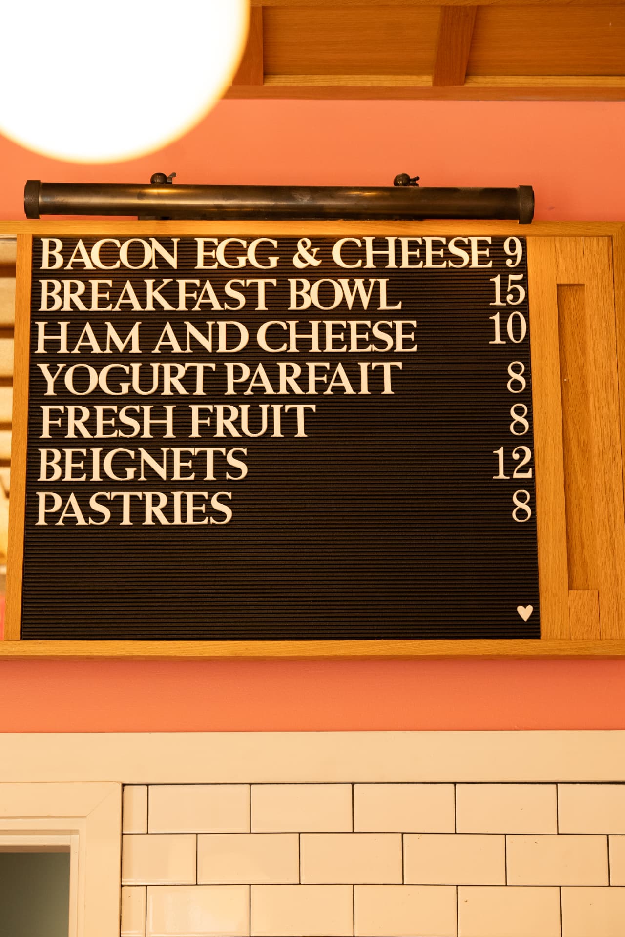 Hand-lettered menu board listing bacon egg and cheese, breakfast bowl, ham and cheese, yogurt parfait, fresh fruit, beignets and pastries