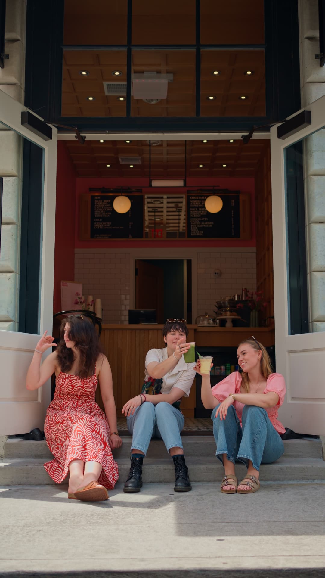 Three friends sitting on the entrance steps with iced matcha and iced tea