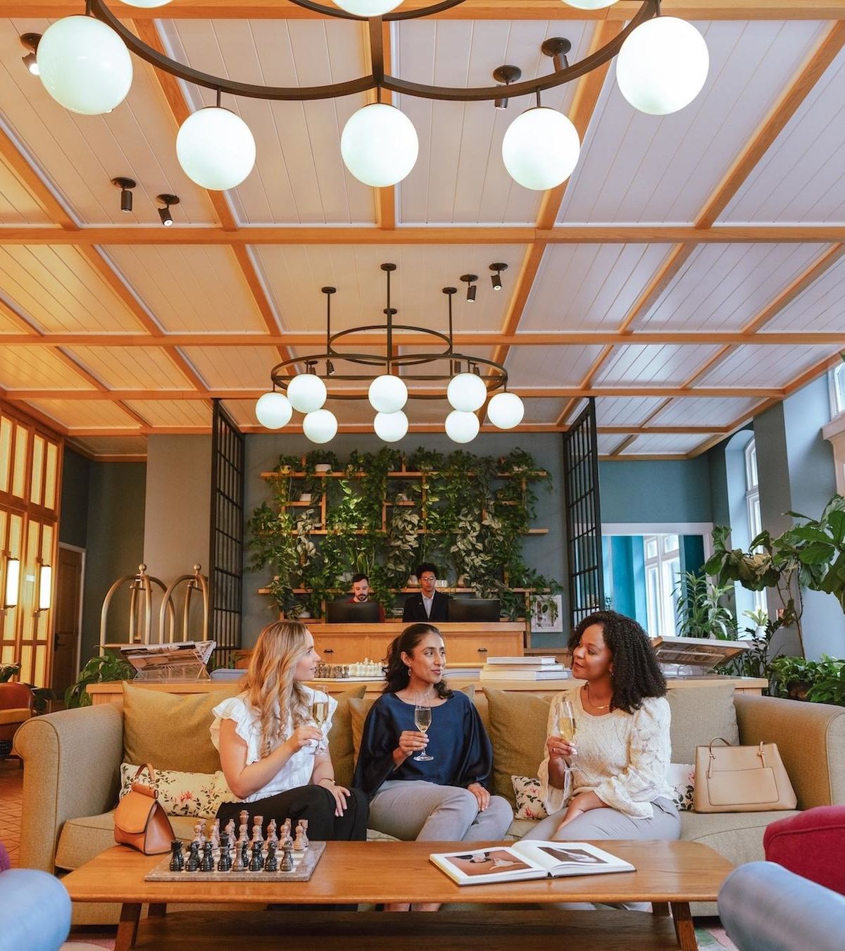 Guests with drinks on the sofa in The Drayton's Living Room lounge, front desk and plant wall behind