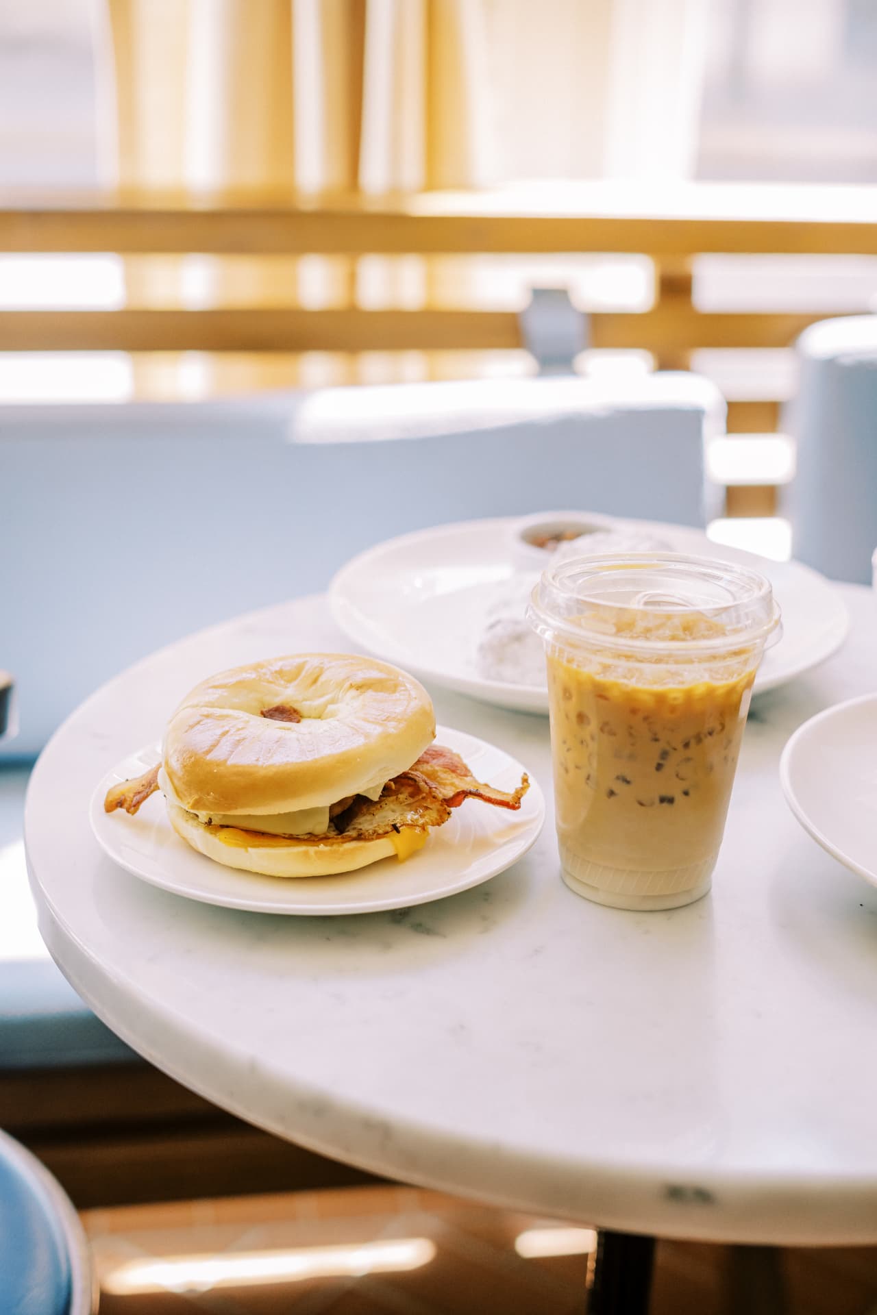 Bacon, egg and cheese bagel sandwich with an iced coffee on a marble bistro table at Corner Coffee