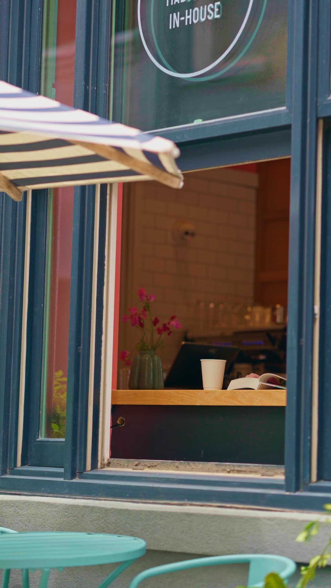 Looking through the open window to a wooden ledge with a coffee cup, an open book and a vase of pink flowers